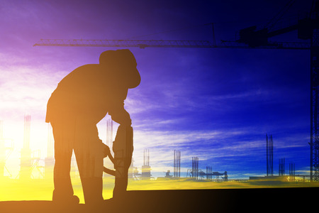 Double exposure of silhouette construction worker repairing the roof with electric drill with construction site backgroundの写真素材
