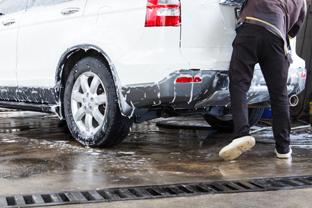 Worker washing white car at the car wash shop to clean up dirt and keep the health of the driver and passengers.の写真素材