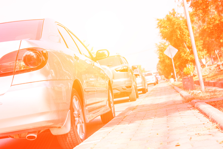 Car parked outdoor in the parking lot beside the sidewalk with peaking sun flare effectの写真素材
