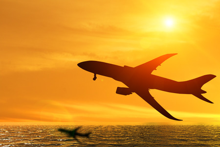 Silhouette of airplane taking off flight with orange sky background over the oceanの写真素材