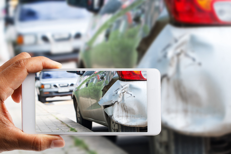 Car insurance agents take pictures of accident-damaged vehicles with a smartphone as a proof of insurance claimの写真素材