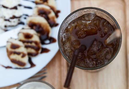 Top view of ice coffee americano with waffles and banana in backの写真素材