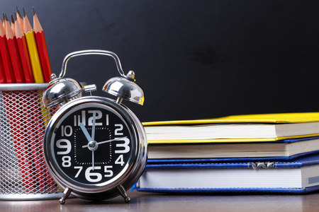 Educational equipment consists of an alarm clock at 11, notebook and pencil placed on a black backdrop study tableの写真素材
