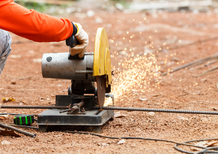 Worker with red shirt cut steel by using electric steel cutting machine on the ground in sunny day with natural backgroundの写真素材