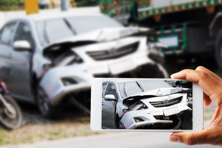 Close up hand holding smartphone and view photo of car accidentの写真素材