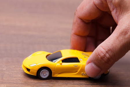 Yellow car toy in the men's hands on wooden backgroundの写真素材