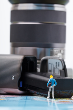 Mini people model in the suit wear a sweater, checking the availability of the battery digital camera before traveling.の写真素材