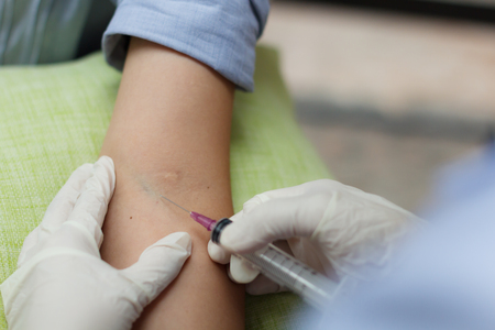 Close up nurse pricking needle syringe in the arm woman patient drawing blood sample for blood testの写真素材