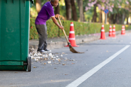 Green trash bin with cleaning worker sweeping garbage on the road backgroundの写真素材