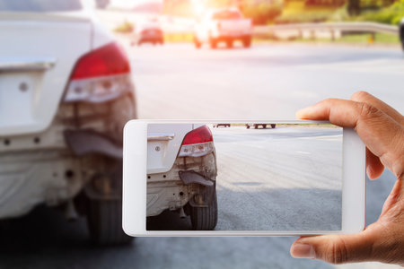 Car insurance agents take pictures of accident-damaged vehicles with a smartphone as a proof of...