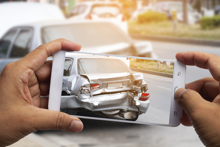 Car insurance agents take pictures of accident-damaged vehicles with a smartphone as a proof of insurance claim.の写真素材