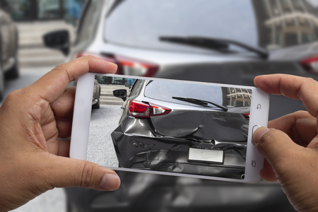 Car insurance agents take pictures of black car accident-damaged vehicles with a smartphone as a proof of insurance claim.の写真素材