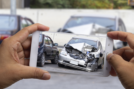 Car insurance agents take pictures of silver accident-damaged vehicles with a smartphone as a proof of insurance claim.の写真素材
