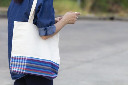 Asian woman carry simple flax eco shopping bag with smart phone, concept of plastic free sign.の写真素材