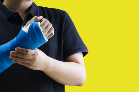 Close up man holding hand with blue bandage as arm injury concept. Isolated on yellow background with copy space.の写真素材