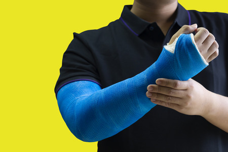 Close up man holding hand with blue bandage as arm injury concept. Isolated on yellow background with copy space.の写真素材