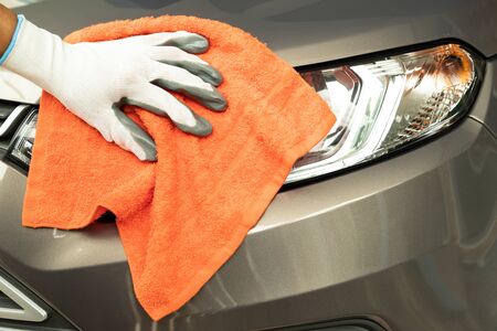 Hand of employees  worker wearing gloves use clean orange micro-fiber cloth to cleaning the car after washing in the car wash shop.の写真素材