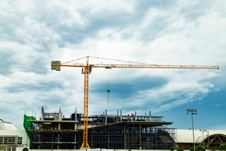 The yellow crane working and minimal labor on the construction site with the blue sky in the...