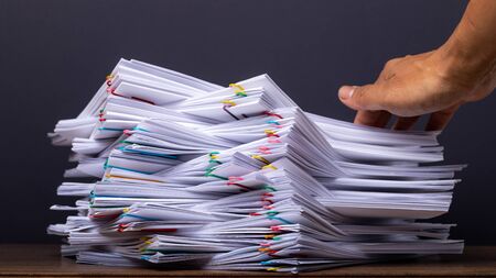 Man hand pick up Stack overload document report paper with colorful paper clip place on black background, business and paperless concept.の写真素材