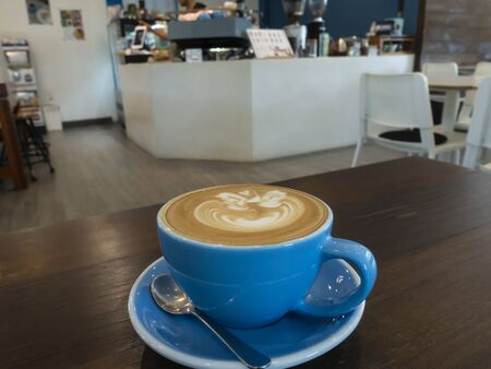 Hot latte coffee cup on wooden table with coffee shop in back,の写真素材