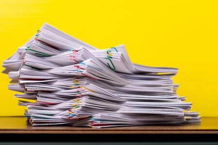 Stack overload document report paper with colorful paper clip place on yellow background, paperless business concept.の写真素材