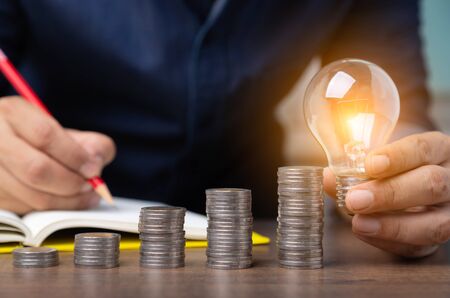 business man hand holding light bulb with coins increase, Concept idea saving energy.の写真素材