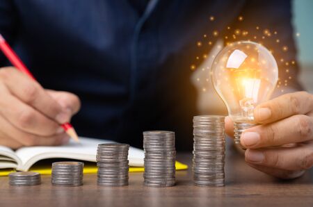 business man hand holding light bulb with coins increase, Concept idea saving energy.の写真素材