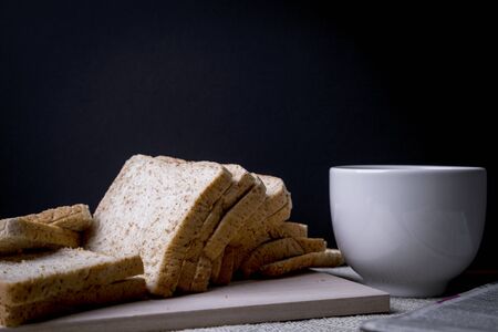Homemade slide bread with hot coffee cup and newspaper on the wooden with copy space on black background.の写真素材