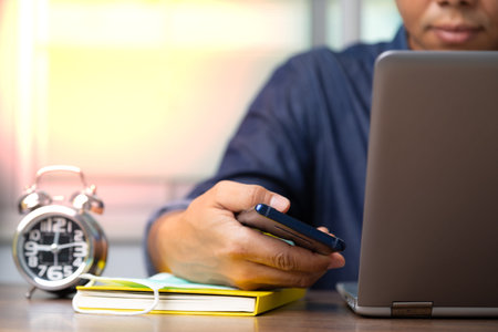 Male employee with cell phone and laptop working from home for preventing corona virus covid-19,...