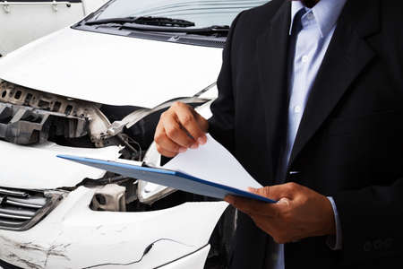 Side view of insurance officer writing on clipboard while insurance agent examining black car after accident.の写真素材