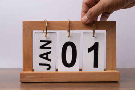 January 1st. Day 1 of january month, hand with calendar on wooden table and white background.