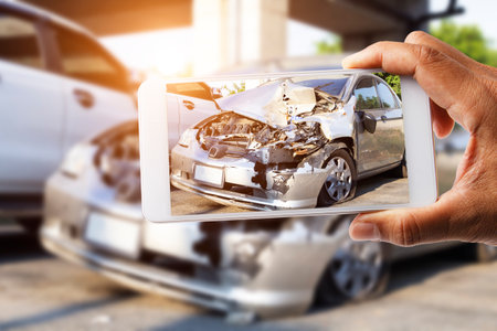 Car insurance agents take pictures of accident-damaged vehicles with a smartphone as a proof of insurance claim.の写真素材