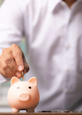 Vertical man hand putting coins into the piggy bank savings, business concept.の写真素材