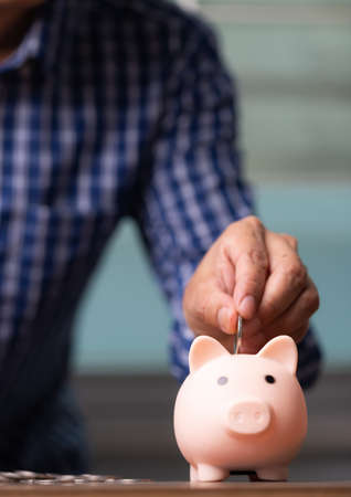 Vertical business man hand putting coins into the piggy bank, saving money concept.の写真素材