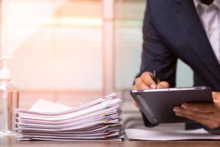 businessman in a suit is writing down the report paper document saving information on the tablet, business concept.の写真素材