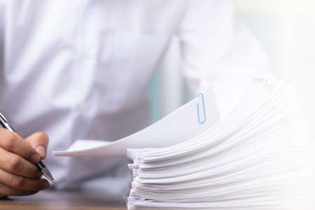 Male office workers holding and writing documents on office desk with light fair, Stack of business overload paper.の写真素材