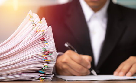 Business man hand writing on Stack overload document report paper with colorful paperclip, business and paperless concept.の写真素材