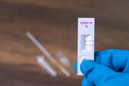Hand with glove holding Rapid kits of Covid-19 Ag test or ATK seen on wooden background with copy...