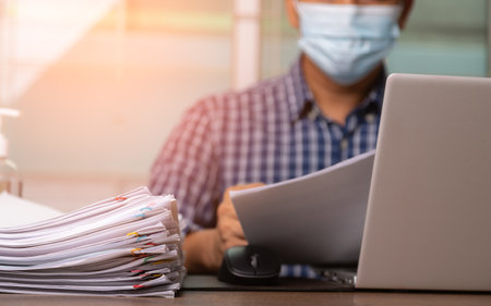 Male office workers with shirt and health mask for prevent coronavirus holding documents and computer laptop on office desk, Stack of business overload paper.の写真素材