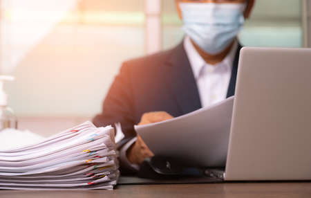Male office workers with suit holding and writing documents and computer tablet on office desk, Stack of business overload paper.の写真素材