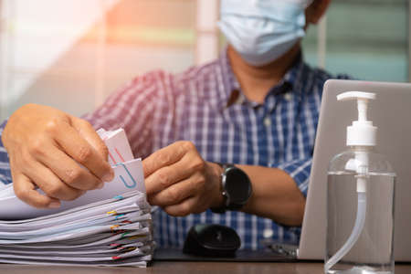 Male office workers with shirt and health mask for prevent coronavirus holding documents and computer laptop on office desk, Stack of business overload paper.の写真素材