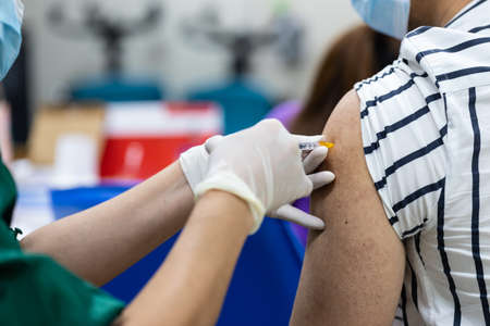 close up of doctor hand holding syringe and using cotton before make injection to patient in medical mask. Covid-19 or coronavirus vaccine, health care concept.の写真素材