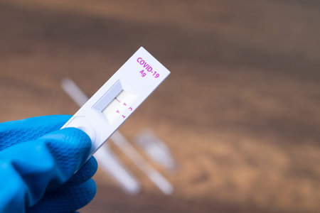 Hand with glove holding Rapid kits of Covid-19 Ag test or ATK seen on wooden background with copy...