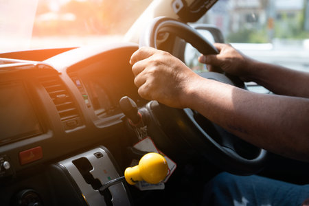 Close up view of man hands holding steering wheel driving car on city street on daytime.