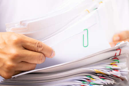 Close-up hands of a man in a white shirt searching for contract agreement documents in Stack of Group report papers clipped in color clipst, business, legal law and education concept.の写真素材