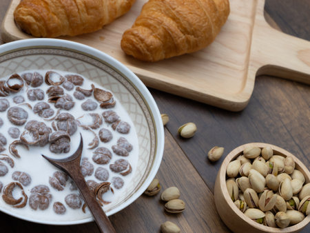Close-up of breakfast cereal with milk, croissants and pistachios on wooden background, healthy food concept.の写真素材