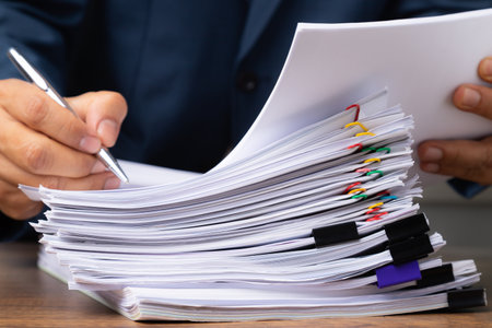 Business man hand writing on Stack overload document report paper with colorful paperclip, business and paperless concept.の写真素材