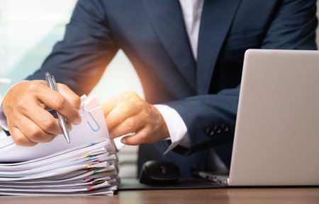 Business man suit holding and writing documents and computer laptop on office desk with copy space, Stack of business overload paper.の写真素材