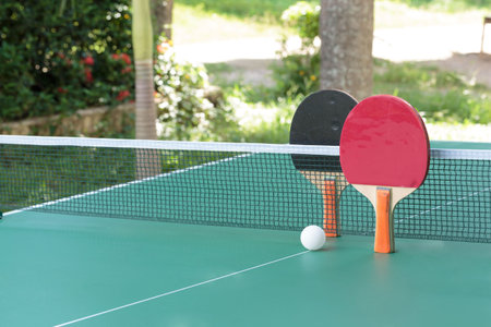 Two table tennis or ping pong rackets and balls on a green table with net