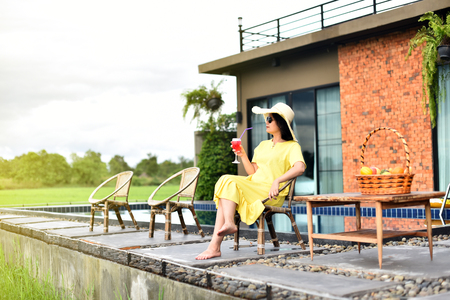 Portrait of Asian woman wear yellow dress sitting near swimming poolの写真素材